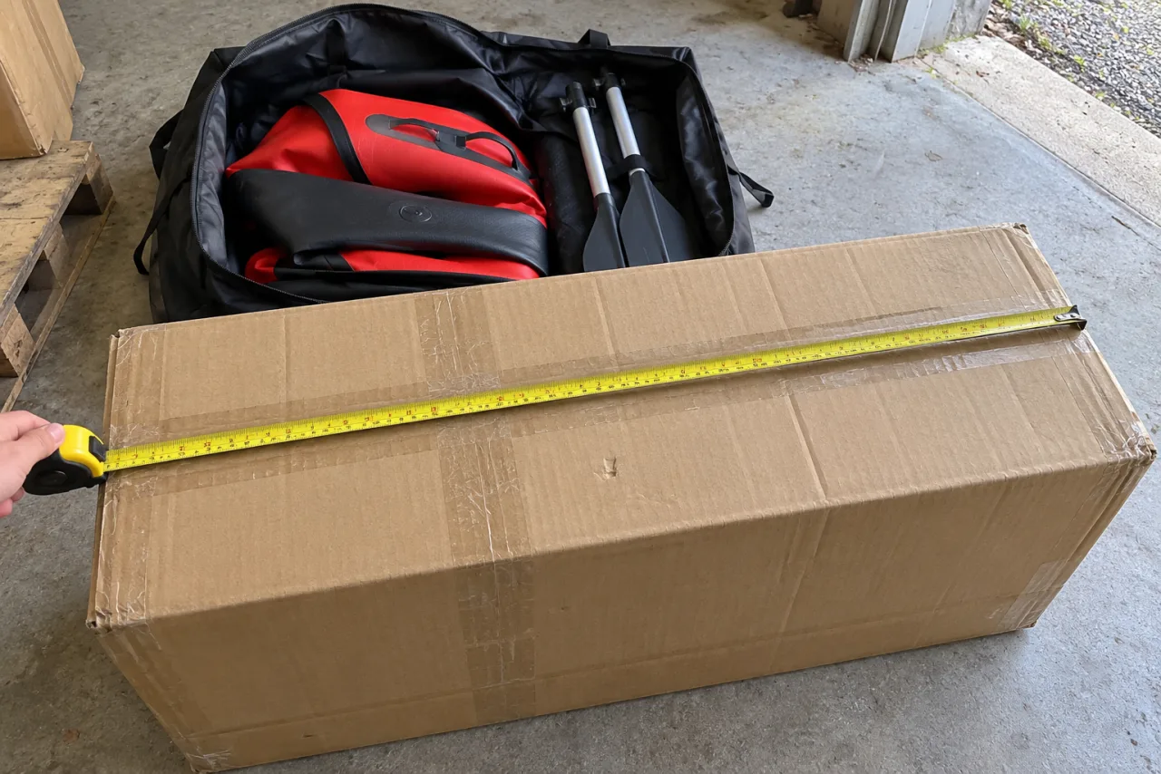 Plain shipping carton with tape measure beside a bag and bundled oars