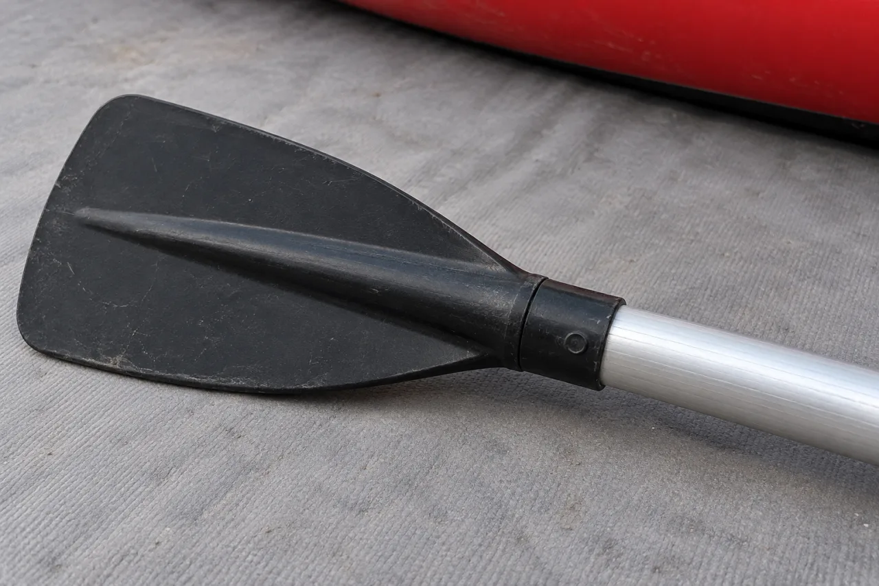 Black oar blade and silver shaft joint resting loose on a gray mat